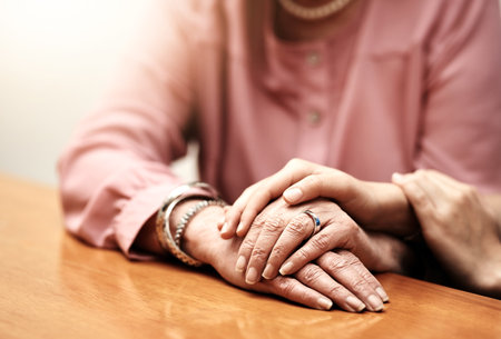 Kindness, support and hands of people on table for compassion, empathy and comfort in hope together. Home, trust and women with gesture of love on desk for forgiveness, understanding and solidarityの写真素材