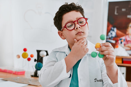 Boy, lab coat and molecule model in classroom with thinking, glasses and learning for development....