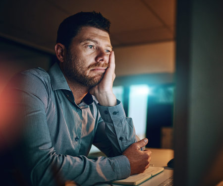 Bored, night and business man at desk by computer for fatigue, overtime or project deadline in...
