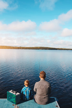 Fishing, together and back of man and son at lake in summer for vacation and relax in morning. Family, father and kid in nature by water for holiday, learning or gear for outdoor adventure with dadの写真素材
