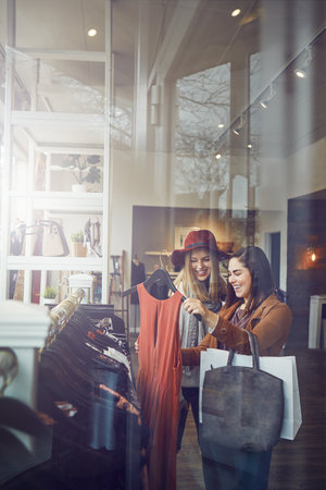 Shopping, store and girl friends with dress in retail mall for discount, sale or promotion. Style, window and young women bonding and buying designer outfit on rack at luxury fashion boutique.の写真素材