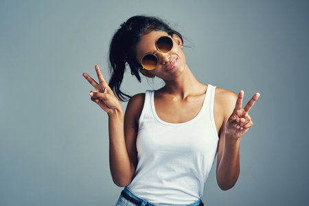 Studio, Indian woman and peace sign with smile, confidence and trendy accessory as sunglasses. Female model, hand gesture and pride with emoji reaction, v symbol and mockup by gray backgroundの写真素材
