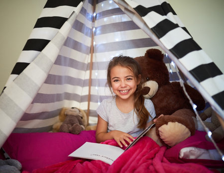 Portrait, happy child and reading book in home tent for education, development or creative knowledge in bedroom. Face, girl and studying fantasy story, information or hobby with teddy bear in houseの写真素材