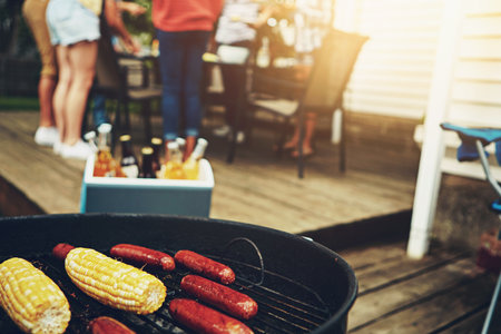 Food, barbecue and outside on weekend with grill for corn, sausage and cooking on porch or backyard. Friends, drinks and dinner party with reunion, meal and summer in America with alcohol for people.の写真素材