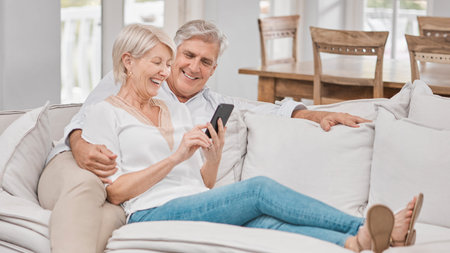 Relax, mobile and senior couple on sofa for social media, browsing internet or reading article in living room. Online, happy woman and elderly man for love, retirement or entertainment in homeの写真素材