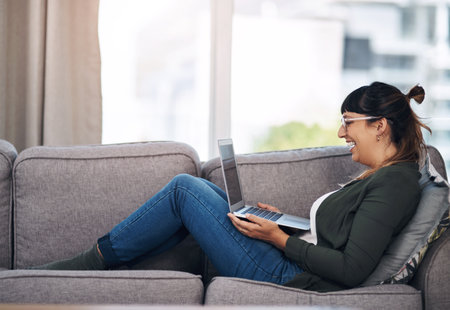 Woman, laptop and relax with laugh on couch for streaming, movie and subscription on web in home living room. Person, smile and computer on sofa for film, series or excited for funny comedy in Mexicoの写真素材
