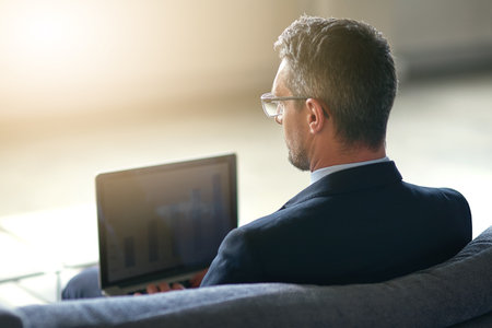 Businessman, laptop and financial charts for stock market research or brainstorming, graphs or analytics. Male person, back and trading investment or economy review for pattern, data or statisticsの写真素材