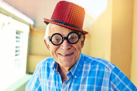 Portrait, smile and sunglasses with senior man in hallway of retirement home for goofy party on weekend. Face, funny and eyewear with happy mature person with crazy outfit in elder care apartmentの写真素材