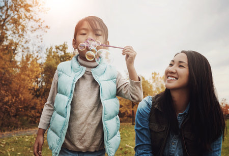 Mom, girl and blowing bubbles in park with smile for fun, playing and bonding with child development. Asian parent, woman and happy with kid in garden on break for care, support and trust as familyの写真素材