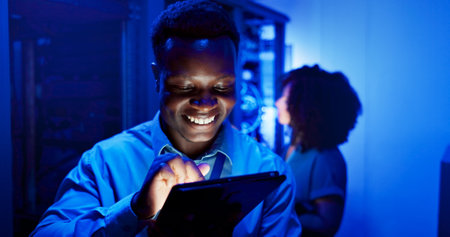 Man, tablet and server room at night for technology, maintenance in dark data center with neon. Male person, digital information and cloud computing with app, network programming or problem solvingの写真素材