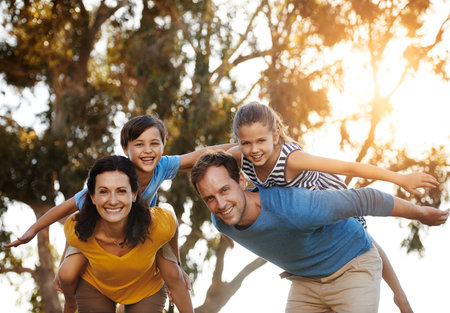 Portrait, family and piggyback children at park for love, care or bonding together in nature. Mother, father or carry kids at garden for airplane game, support or happy parents play on summer holidayの写真素材