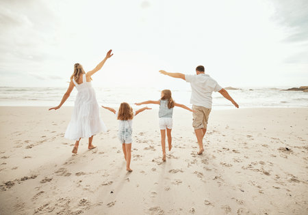 Beach, airplane and family running in nature with freedom, vacation and love at ocean. Travel, energy and back of children with parents at sea for flying games, support and having fun while bondingの写真素材