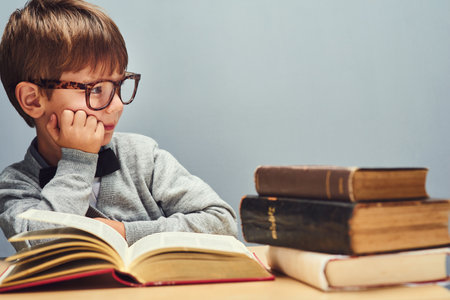 Boy, books and education in studio with space for mockup, glasses and thinking for learning by blue background. Child, textbook and vision for future, study and scholarship for development at academyの写真素材