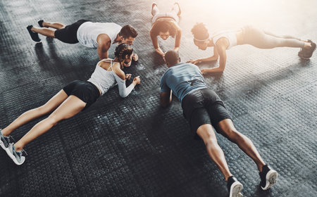 Class, training and plank in group at gym for workout, core exercise or fitness together indoors. Diverse people, friends and warm up for ab muscle, session and sport for health on gymnasium floorの写真素材