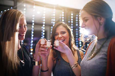 Friends, happy and shots in club for party, event or nightlife, bonding and friendship with fun or laughter. Woman, alcohol and nightclub with excitement for celebration, birthday and social drinkの写真素材