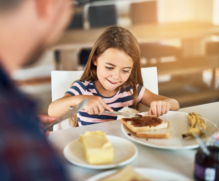 Breakfast, bread and daughter with dad, smile or morning in kitchen, butter and dining table in home. Healthy, father and food of family, child and man in house, eating and bonding with love togetherの写真素材