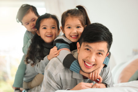 Asian family, portrait and dad with kids on bed for bonding together, support and growth in bedroom. Father, girl children and happy with love, healthy relationship and development in Singapore homeの写真素材