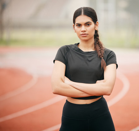 Woman, portrait and arms crossed at stadium for exercise, runner and training in outdoor for fitness. Female person, confidence and athlete for marathon or competition, arena track and start of raceの写真素材