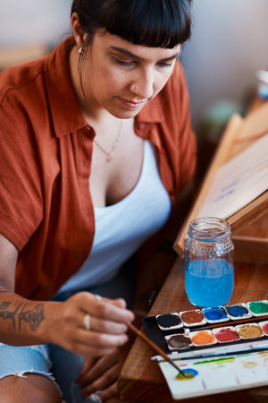 Brush, paint and woman in home for creativity with skill, weekend project and craft talent. Small business, painter tool and entrepreneur artist with watercolor palette for painting and art galleryの写真素材