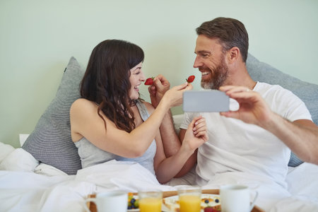 Couple, relax and selfie with fruit in bedroom, bed and breakfast for rental on honeymoon vacation...