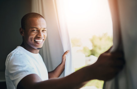 Morning, curtains and black man with smile, window and wake up in sunrise, vacation and happy in hotel. Business, trip and hospitality for accommodation in Nigeria, summer or ready for meetingの写真素材