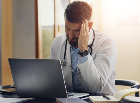 Headache, healthcare and laptop with doctor in hospital of office for medical report or research. Anxiety, burnout and computer with medicine professional in clinic for cardiology or problem solvingの写真素材