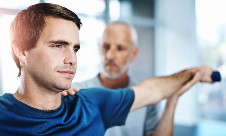 Physiotherapy, man and arm with stretching in clinic for rehabilitation, treatment and support. Orthopedic, service and people with exercise in office for injury, assessment or consulting on progressの写真素材