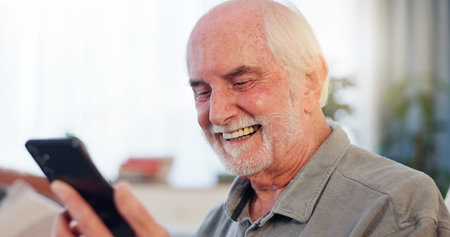 Senior man, retirement home and excited with smartphone for online gambling with rewards and winning. Sofa, living room and smile or happy for website or mobile app for games, social media and memesの写真素材