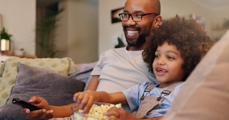 Father, boy and happy with television or popcorn on sofa in living room for movies, cartoon and...