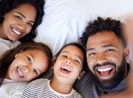 Happy family, portrait and relax with children for selfie, memory or photography on bed at home. Father, mother and kids lying in bedroom with smile for morning, moment or picture together at houseの写真素材