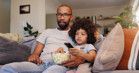 Dad, boy and watching movie with popcorn on sofa in living room for movies, cartoon and entertainment. People, parent and kid with television on couch for streaming or subscription and childcareの写真素材