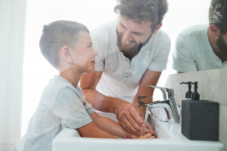 Bathroom, father and child washing hands with soap, smile and teaching healthy hygiene in mirror. Cleaning, dirt and germs on fingers with happy boy, dad and morning wellness for skincare in home.の写真素材