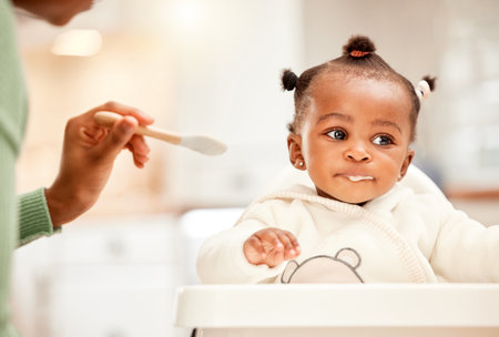 Baby, hands of mom and feeding chair in kitchen for nutrition, growth or support in home. Food, child or parent in morning for breakfast, routine or hungry with meal for development, care or healthの写真素材