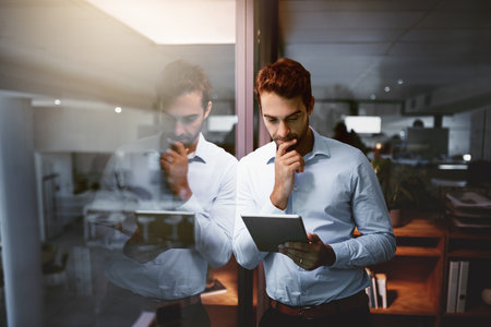 Businessman, tablet and night with thinking, research and overtime work and data analysis. Web designer, technology and database for man, cloud computing and b2b networking for online communicationの写真素材