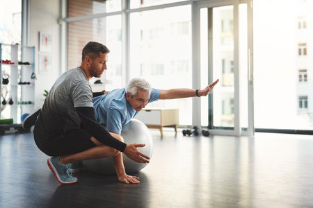Stretching, elderly man and physiotherapist with ball for mobility training, support or muscle workout. Fitness, physiotherapy and senior person with exercise, development or healthcare in retirementの写真素材