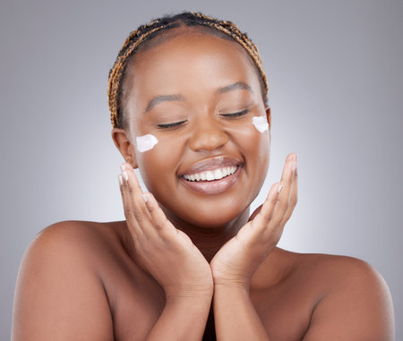 Cream, beauty and face of black woman in studio for skincare, wellness and facial care on white background. Dermatology, salon and isolated person with moisturizer, lotion and anti aging cosmeticsの写真素材