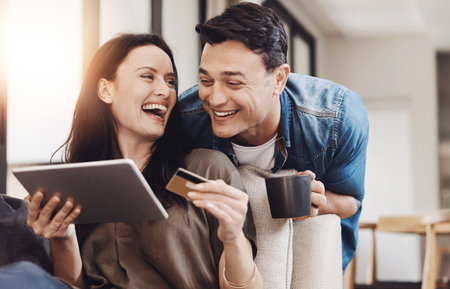 Online shopping, tablet and happy couple on sofa with credit card, coffee and savings for home budget. Fintech, woman and man on couch with smile, financial freedom and digital app for payment plan.の写真素材