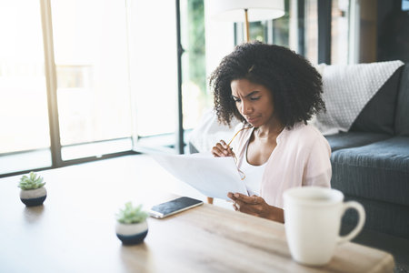 Confused, finance and mortgage with woman reading documents in living room of home for accounting or planning. Bank, loan and tax with person in apartment for investment or savings informationの写真素材