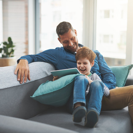 Dad, tablet and child with laughing on sofa for funny show, entertainment and bonding together. Family, home and son with tech by man for online comedy, streaming and watching cartoon in living roomの写真素材