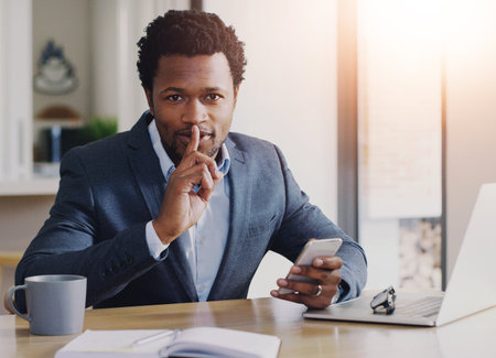 Secret, portrait and businessman with phone in office for illegal strategy on stock market investment. Quiet, cellphone and African male broker with laptop for private foreign exchange trading.の写真素材