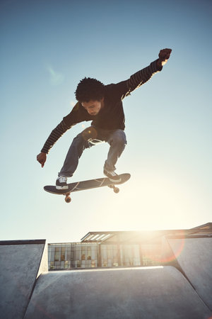 Skateboard, man and jump in city skate park with trick and training in Los Angeles with exercise. Sunshine, deck and skater with balance, sport competition and fun board flip by ramp in cityの写真素材