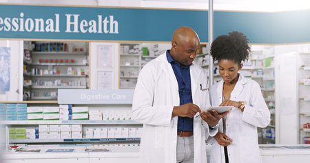 Pharmacist, reading and team with tablet for inventory, pharmaceutical stock or medical check at pharmacy. Black man, woman or employees with technology for online service or telehealth at dispensaryの写真素材