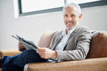 Portrait, mature man and relax with newspaper for current event update, information and morning article at house. Smile, male person and newsletter, magazine story or media knowledge of daily routineの写真素材