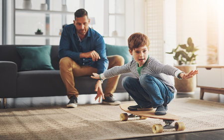 Father, child and skateboard with balance in living room for activity, leisure or skill at home. Dad, kid or little boy riding on board with wheels for bonding, holiday or weekend together at houseの写真素材