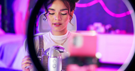 ASMR, relax and influencer woman with microphone, ring light and audio content creator in neon home...