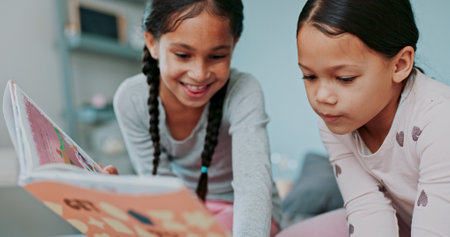 Girls, kids and happy in bedroom with book for storytelling with bonding, education and child development. Home, sisters and smile with reading fantasy for knowledge, literacy and learning on growthの写真素材