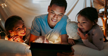 Reading, night and tablet with family in bedroom of home together for bonding, love or storytelling. Education, learning or relax with father and sister kids on bed in apartment for child developmentの写真素材