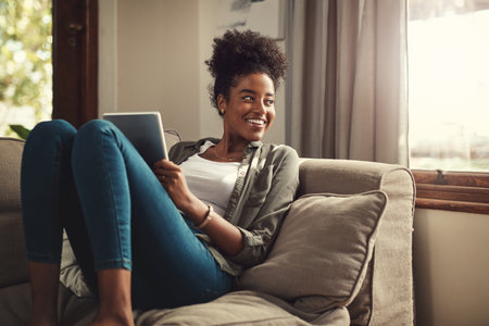 Happy, tablet and black woman on sofa in morning for social media, online shopping and internet. Relax, window and person on digital tech for website, news and research on weekend in living roomの写真素材