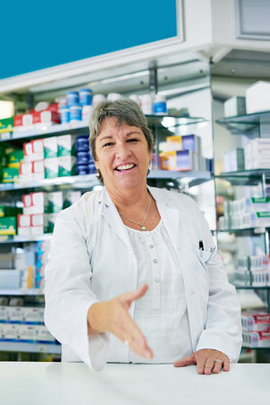 Woman, handshake and pharmacist or mature portrait, trust and drug store in medication dispensary. Healthcare, worker and medicine retailer, welcome gesture and introduction with professionalの写真素材