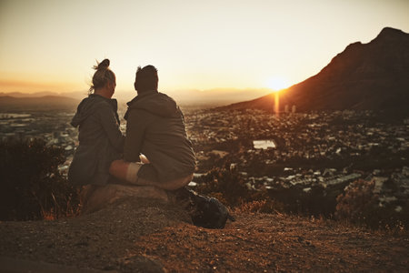 Couple, hiking and sunrise on mountain with relax for morning adventure, scenery and explore with bonding. Back, people and trekking on expedition for sightseeing, love or together on cliff in natureの写真素材
